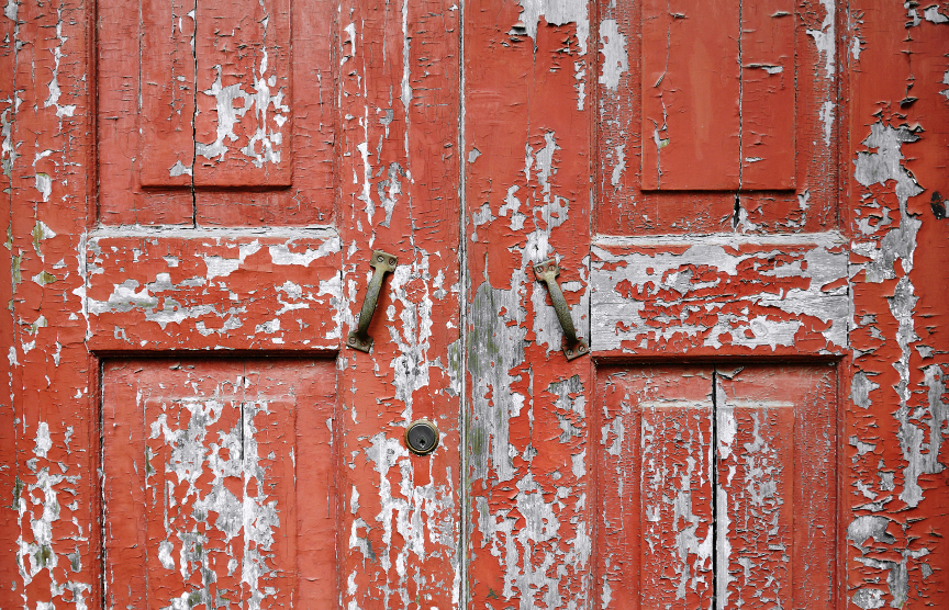 Wooden double door with flaking red paint and cracks
