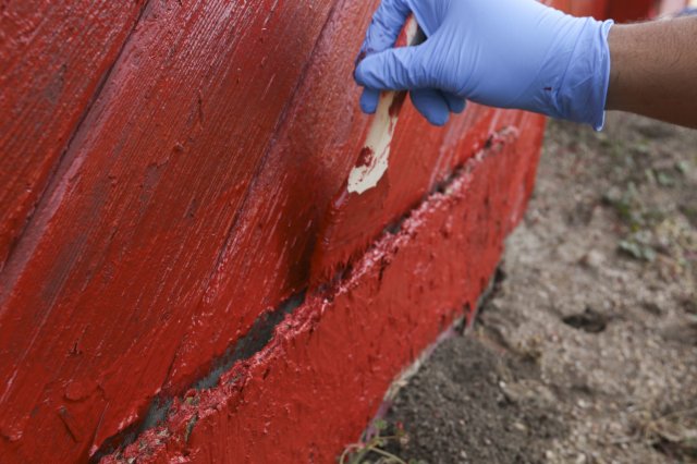 Close-up image of a door being painted by a gloved hand in red paint